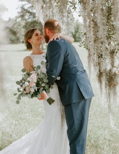 Couple poses for a portrait under an oak tree draped in Spanish moss at C Bar Ranch near Gainesville, Florida. Photo by Amyreneephotographs.com