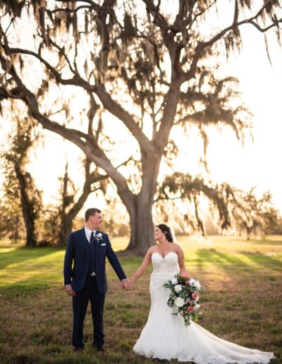 A bride and groom hold hands under towering oak trees at C Bar Ranch, an award-winning, North Florida wedding venue.