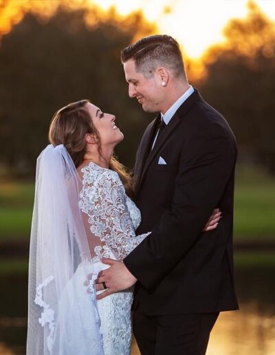 Bride and groom embrace near the C Bar Ranch pond with a flaming sunset behind them.