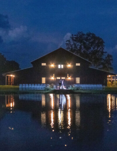 Bride and groom in front of the C Bar Ranch barn with glowing market lights at night.
