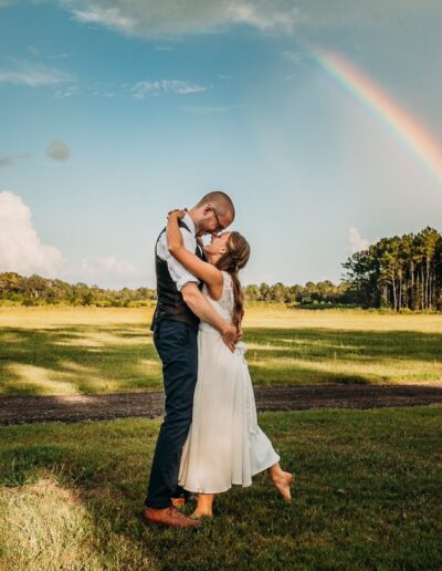 A bride and groom in a grassy field at C Bar Ranch with a bright rainbow behind them.