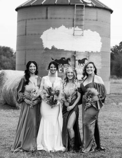 A bride and bridesmaids with flowers in front of a silo with a mural at C Bar Ranch.