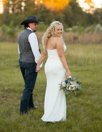 A bride and groom walk through a field at C Bar Ranch at golden hour.