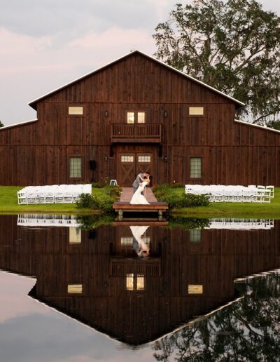 Bride and groom on dock on pond in front of the C Bar Ranch with a mirror image on the pond.
