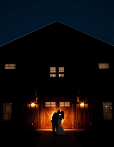 Silhouette of a bride and groom in front of the C Bar Ranch barn at night.